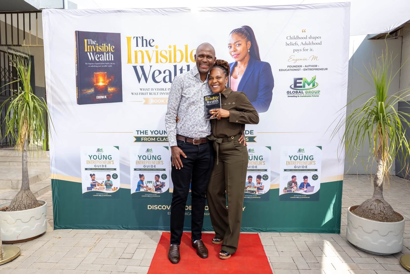 Eugenia M. with a guest, holding The Invisible Wealth in front of the launch backdrop
